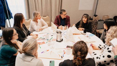 A table of attendees from Putting Patients First 2024, in the arts-based activity room. On the table in front of them are folded origami hats.