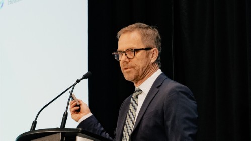 Robert Reid speaking into a microphone, while holding up a laser pointer.