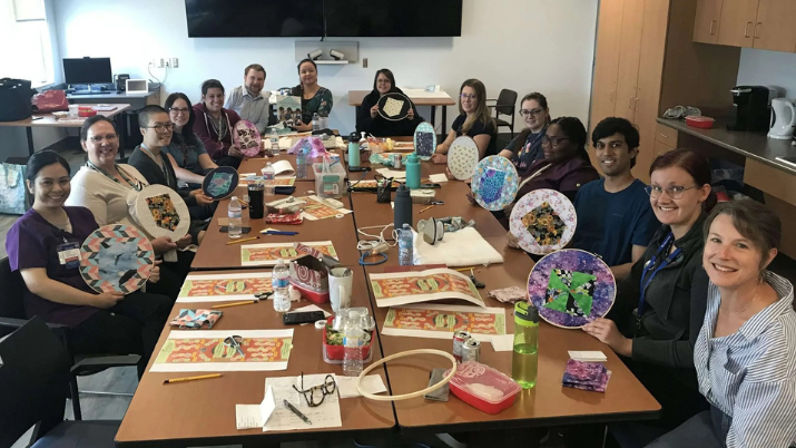 A group of pharmacy staff from Northern Health sitting around a table, smiling and showing their art during a Secret Pocket workshop.