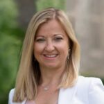 Erika Basile smiling broadly, with what looks like a building and trees behind her