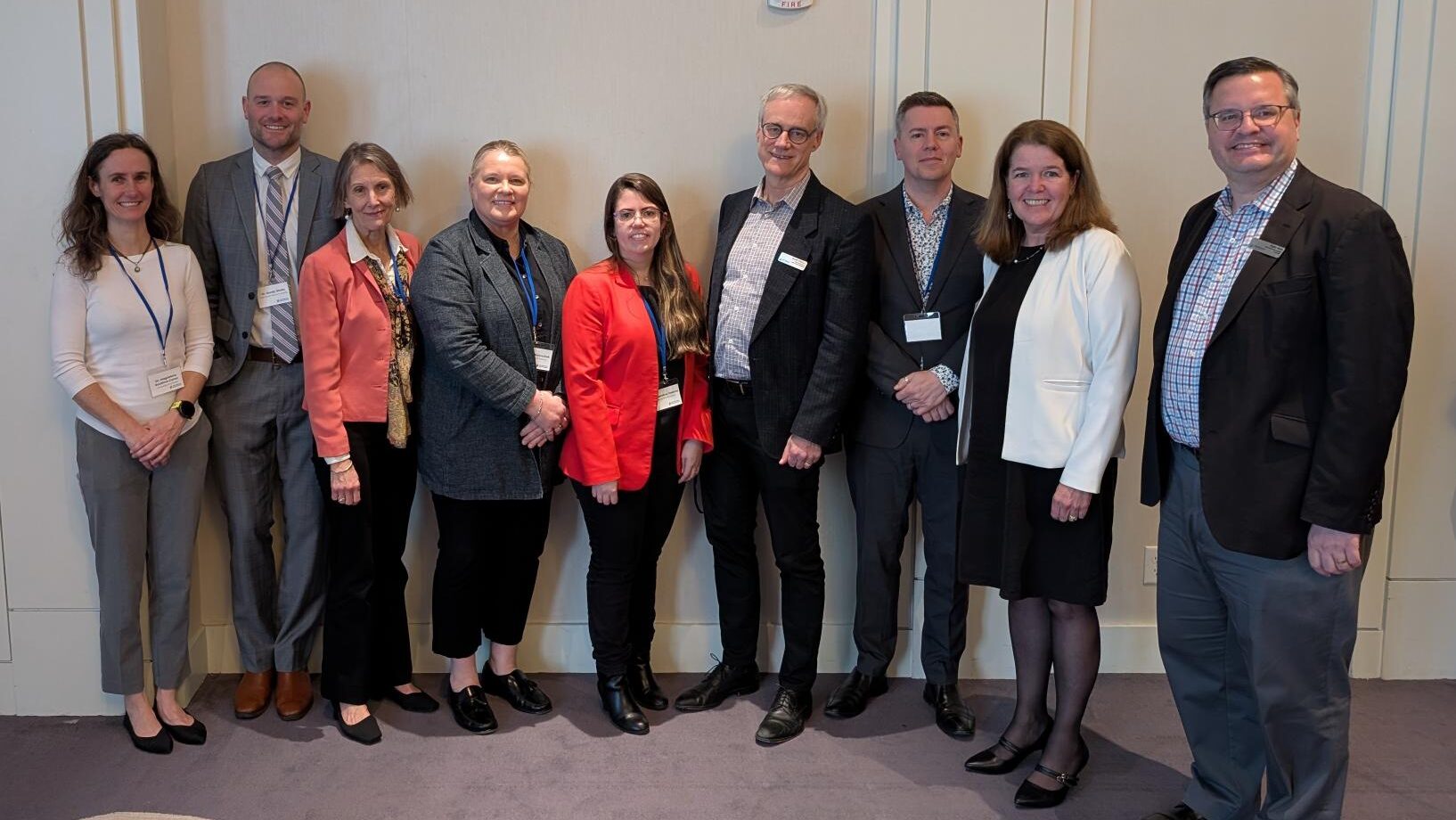 A group of ten professionally dressed individuals standing side by side against a beige wall at the Life Sciences BC’s Showcase Series: Vancouver Island event. Dr. Sandy Shultz is second from the left; on his right is Dr. Bev Holmes, President & CEO of Health Research BC.
