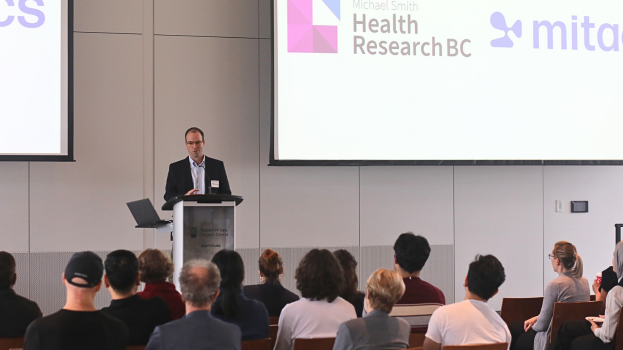 Image of Dr. Nicholas Weilinger speaking in front of audience during the Health Research BC-Mitacs media event in 2025.