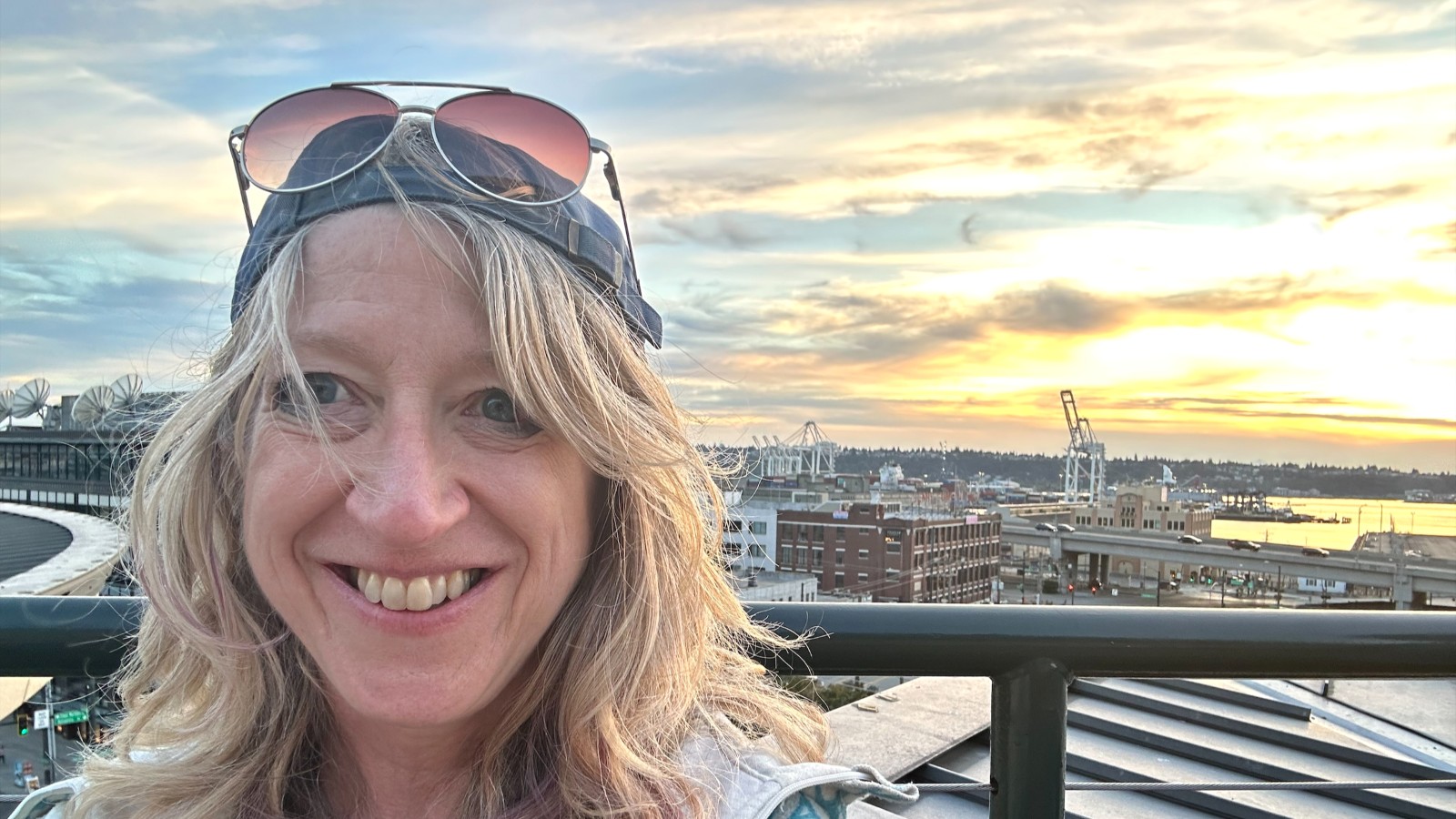 Sarah Greene with sunglasses and a Mariner's cap, against a bright sunset